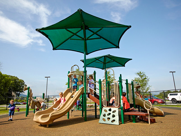 Children playing on an early childhood playground with poured rubber surfacing and two large green shade canopies at Memorial Hospital Children’s Learning Center in Chattanooga Tennessee, installed by Bliss Products and Services.