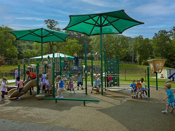 Children playing on an early childhood playground under large green shade structures with poured rubber surfacing at Memorial Hospital Children’s Learning Center in Chattanooga Tennessee, supplied by Bliss Products and Services.
