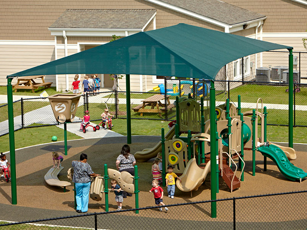 Early childhood playground with slides and climbing structures under a large rectangular shade canopy, designed and installed by Bliss Products and Services.
