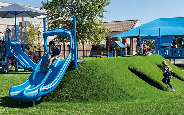 Double slide set into a grassy berm on synthetic turf in a playground in Shorterville. Henry County, Alabama - available from Bliss Products and Services.