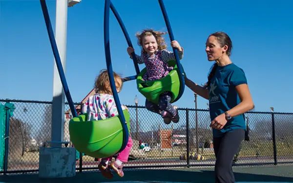 Caregiver assisting children on face-to-face toddler swings, available from Bliss Products and Services.