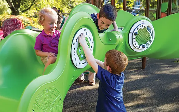 Ground-Level Sensory Play Panel Children engaging with a green ground-level sensory play panel, available from Bliss Products and Services.