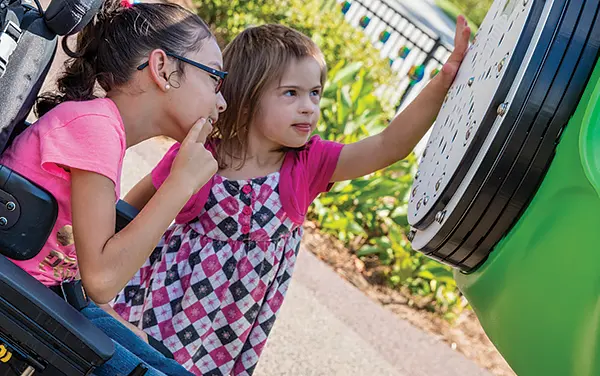 Child in wheelchair with another child playing with interactive feature on playground in Clay County, FL