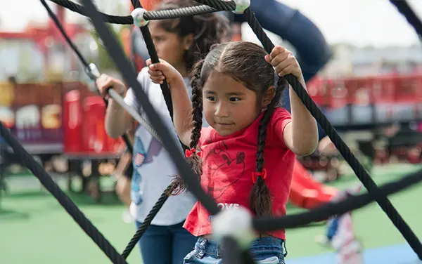 Girl navigating a cargo net play element, available from Bliss Products and Services.