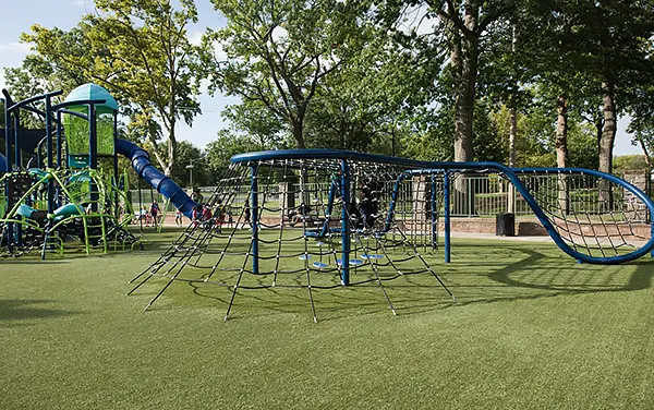 Undulating wave net climber beside a modular playground,.