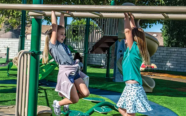 Two girls using an overhead ladder on a playground in Dallas County, Alabama, available from Bliss Products and Services.