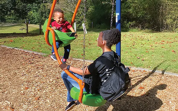 Parent and toddler riding a face-to-face swing over engineered wood fiber in Jefferson County, Alabama, available from Bliss Products and Services.