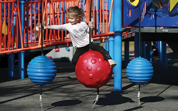 Child navigating a rope ball swing traverse that builds balance and core strength, available from Bliss Products and Services.