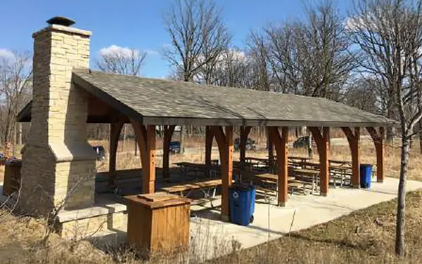 Timber pavilion with a stone fireplace and picnic tables, available from Bliss Products and Services.