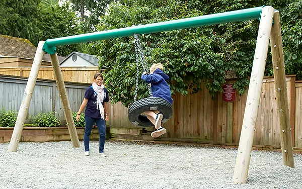 Child on a tire swing supported by wood posts at a playground in Josephine, Alabama, available from Bliss Products and Services.
