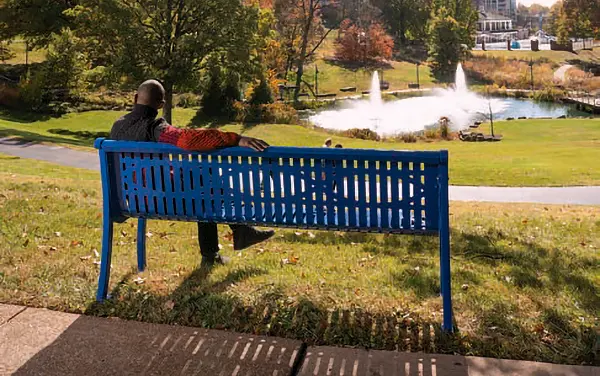 Person on a blue metal park bench with back overlooking a park with fountains in Daphne, AL, available from Bliss Products and Services.