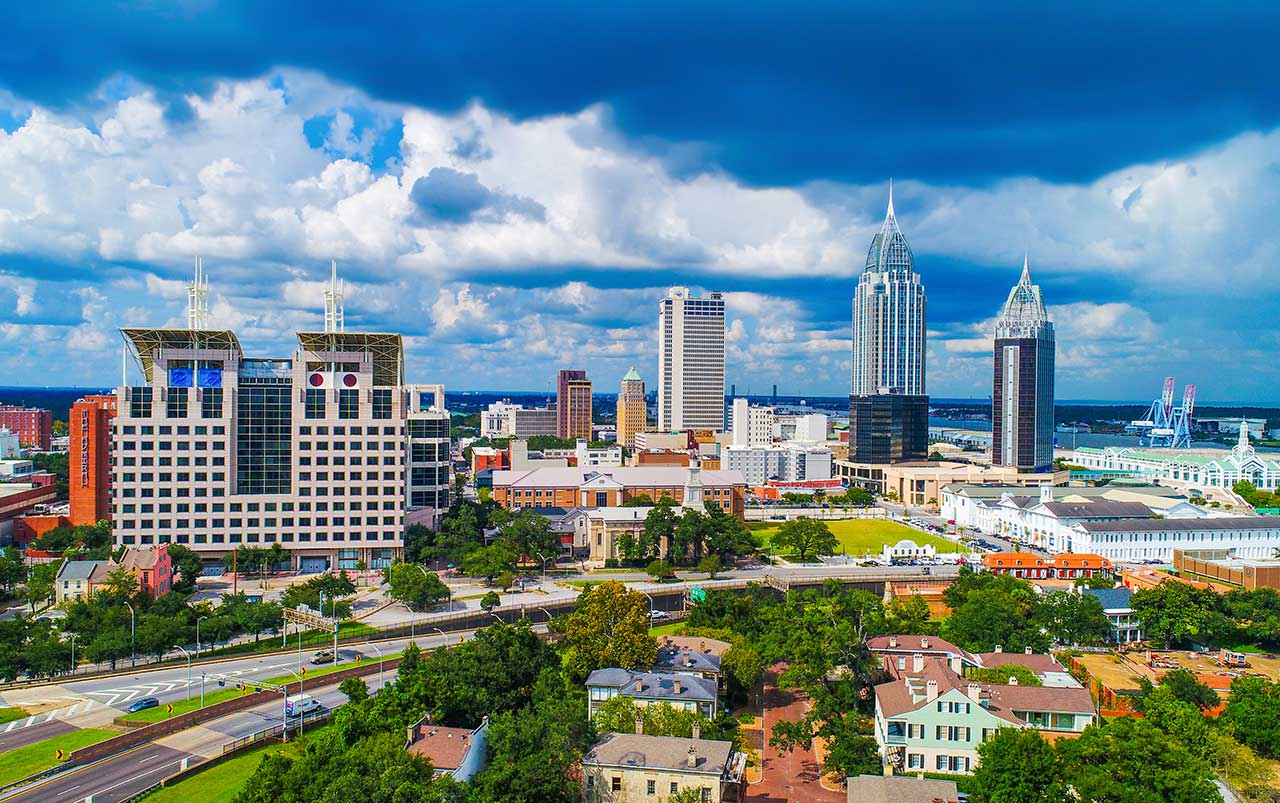 Aerial view of downtown Mobile, Alabama skyline with waterfront and port cranes on the Gulf Coast.