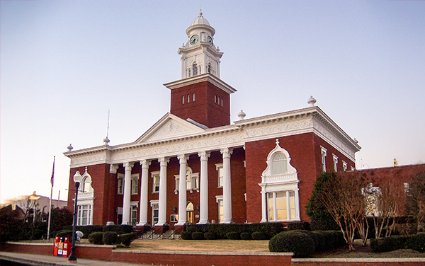 Lee County Courthouse in Opelika, Alabama, red-brick facade with white columns and clock tower. Used by Bliss Products and Services.