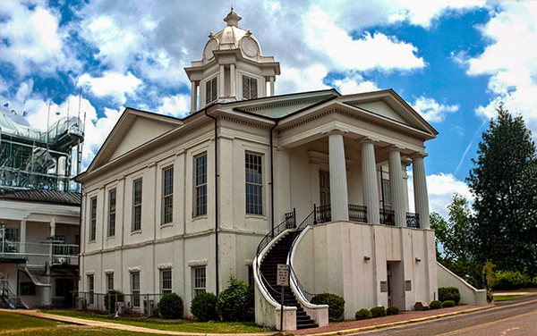 Lowndes County Courthouse in Hayneville, Alabama, white facade with columns and twin curved stairways. Used by Bliss Products and Services.