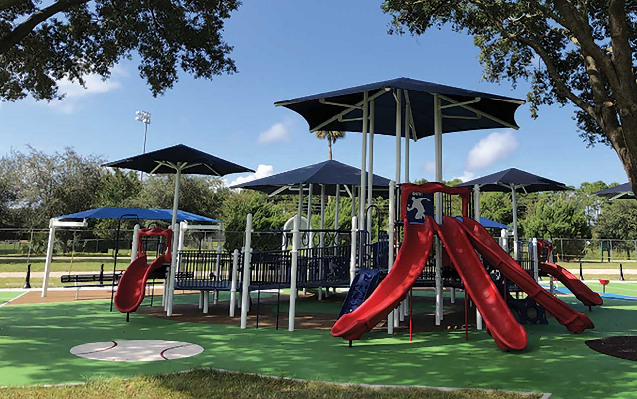Playground with multiple shade canopies and red slides on synthetic turf.