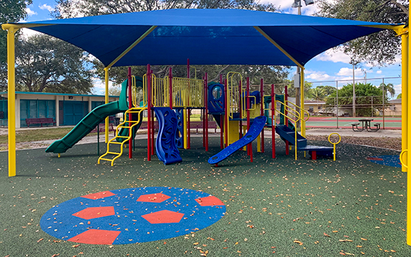 Safety-Surfacing-Mrytle-Grove-Florida- Maroon perforated steel benches with school logos along a walkway.