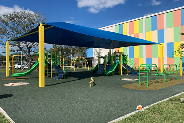 Large blue playground shade canopy over bright play equipment and poured in place rubber surfacing at Bunche Park Elementary in Miami Gardens, Florida, installed with Bliss Products and Services.