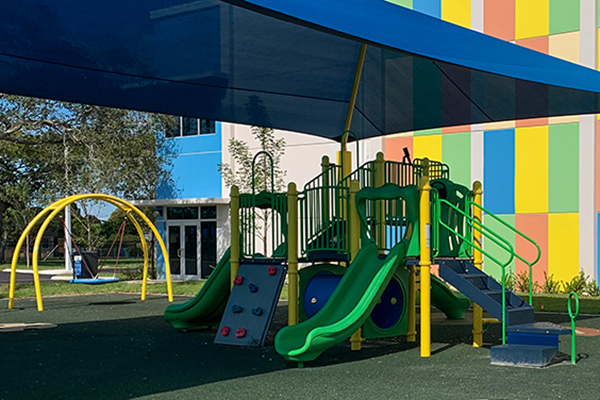 Shaded playground structure with green slides and PIP rubber surfacing at Bunche Park Elementary in Miami Gardens, Florida, installed by Bliss Products and Services.