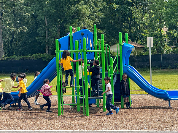 Children playing on a blue and green playground structure in the courtyard at EXCEL Academy in Maryland, installed by Bliss Products and Services.
