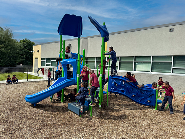 Children playing on a blue and green playground structure in the courtyard at EXCEL Academy in Maryland, installed by Bliss Products and Services.