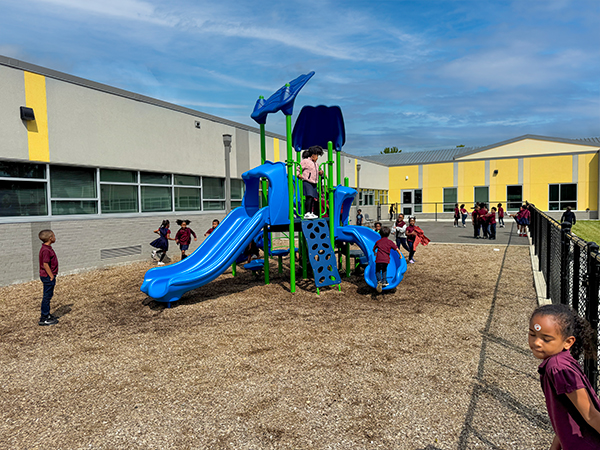 Young students using the double slide and climber on the blue and green playground at EXCEL Academy in Maryland, designed and supplied by Bliss Products and Services.
