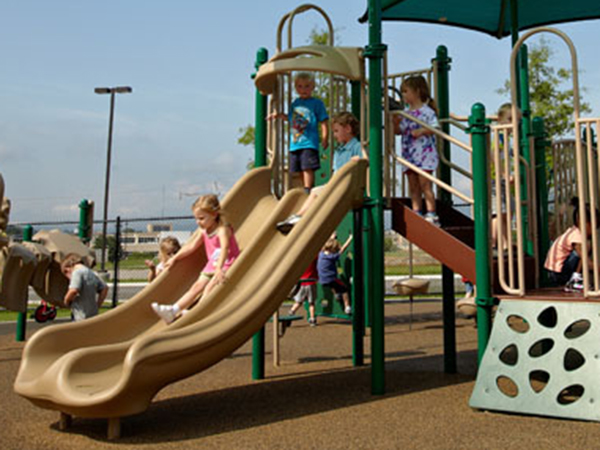 Young children using a tan double slide on an early childhood playground with poured rubber surfacing at Memorial Hospital Children’s Learning Center in Chattanooga Tennessee, supplied by Bliss Products and Services.