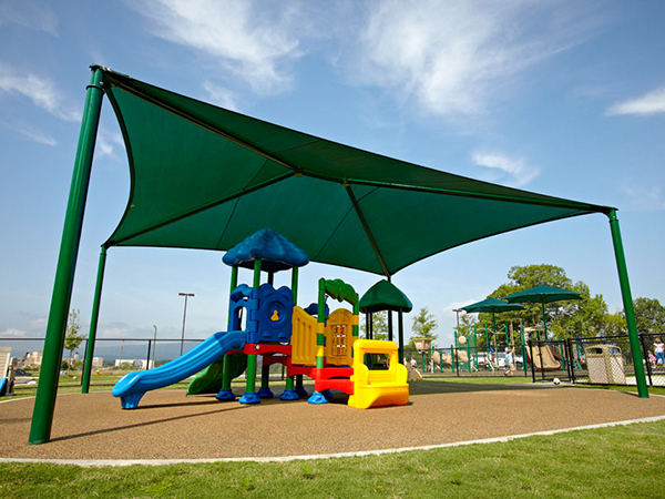Early childhood playground with bright play structure and large green shade canopy by Bliss Products and Services