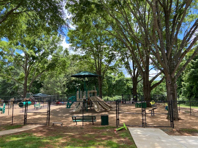 Wide view of fenced playground under mature trees in Clemmons, NC | Bliss Products and Services