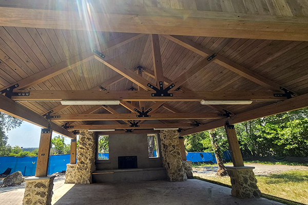 Interior view of the Ben Butler Rock House Pavilion at Charles F. Vollman Park in Hollywood, Florida, showing timber roof trusses, hardware connections, and preserved coral rock chimney wall. Bliss Products and Services.