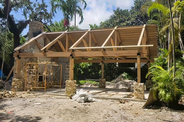 Timber framing and roof structure under construction at the Ben Butler Rock House Pavilion at Charles F. Vollman Park in Hollywood, Florida, alongside the preserved coral rock chimney. Bliss Products and Services.
