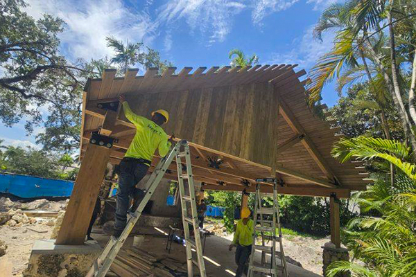 Workers installing exterior timber cladding and roof edge details during reconstruction of the Ben Butler Rock House Pavilion at Charles F. Vollman Park in Hollywood, Florida. Bliss Products and Services.