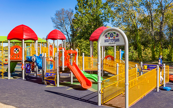 Carter Park playground entry ramp with yellow railings and a Bienvenidos welcome sign | Bliss Products and Services