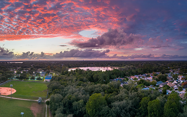Aerial view of Red Bug Lake in Casselberry, Florida with neighborhood homes, sports fields, trees, and a sunset sky.