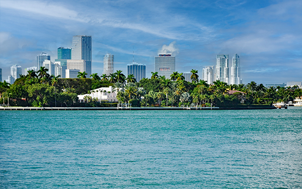 Miami skyline viewed from Biscayne Bay, with waterfront homes, palm trees, and high-rise buildings in Miami-Dade County, Florida.