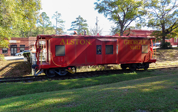 Red historic caboose marked Alston, Georgia, beside railroad tracks in Montgomery County