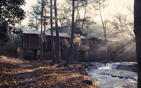 Historic Coheelee Creek Covered Bridge beside flowing water and woodland in Early County, Georgia