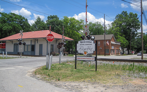 Byron welcome sign, railroad crossing and historic depot on Main Street in Peach County, Georgia, featured by Bliss Products and Services