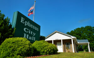 Ephesus City Hall building and roadside sign beneath American and Georgia flags in Ephesus, Georgia.