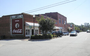 Historic brick storefronts, parked vehicles, street lighting, and a Coca-Cola wall sign in downtown Lincolnton, Georgia.
