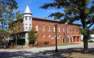 Historic brick commercial building with a corner tower, sidewalks, trees, and street lighting in downtown Louisville, Georgia.