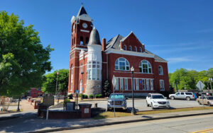 Historic red brick Haralson County Courthouse with clock tower, parked vehicles, trees, and public grounds in Buchanan, Georgia