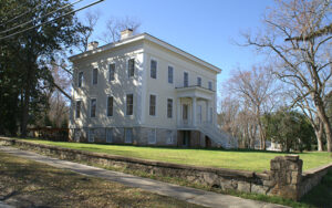 Large historic white house with steps, lawn, stone wall, and mature trees in Sparta, Georgia