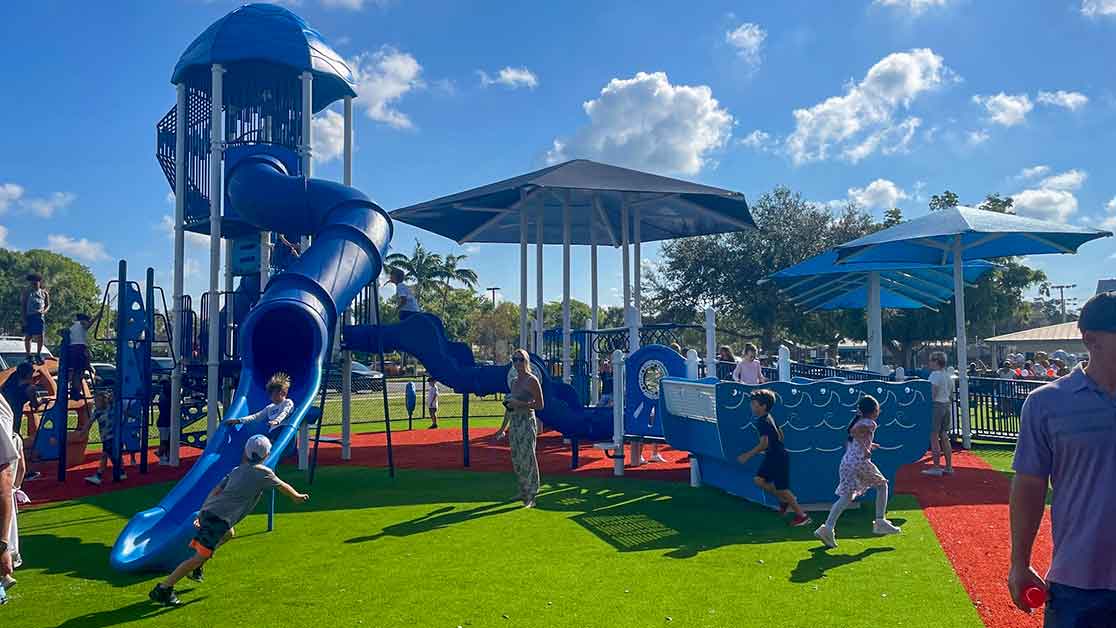 Children playing on the shaded inclusive playground at Fleischmann Park in Naples, Florida