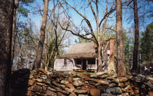 Historic wooden house behind a stone wall and mature trees at Jarrell Plantation in Jones County, Georgia.