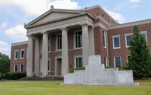 Brick Lamar County Courthouse with tall columns and a stone memorial on the lawn in Barnesville, Georgia.