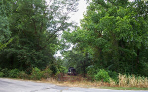 Louisville and Wadley SW-1 locomotive behind a gated, tree-lined railroad crossing in Wadley, Georgia.