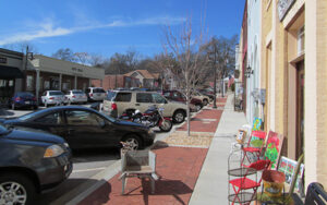 Brick sidewalk, storefronts, outdoor chairs, parked vehicles, and City Hall on Main Street in Flowery Branch, Georgia